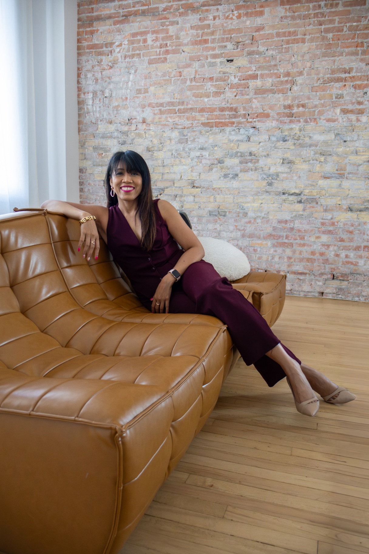 Frances M., founder of The Next Chapter Hub, seated on a leather couch in a warm brick-walled studio